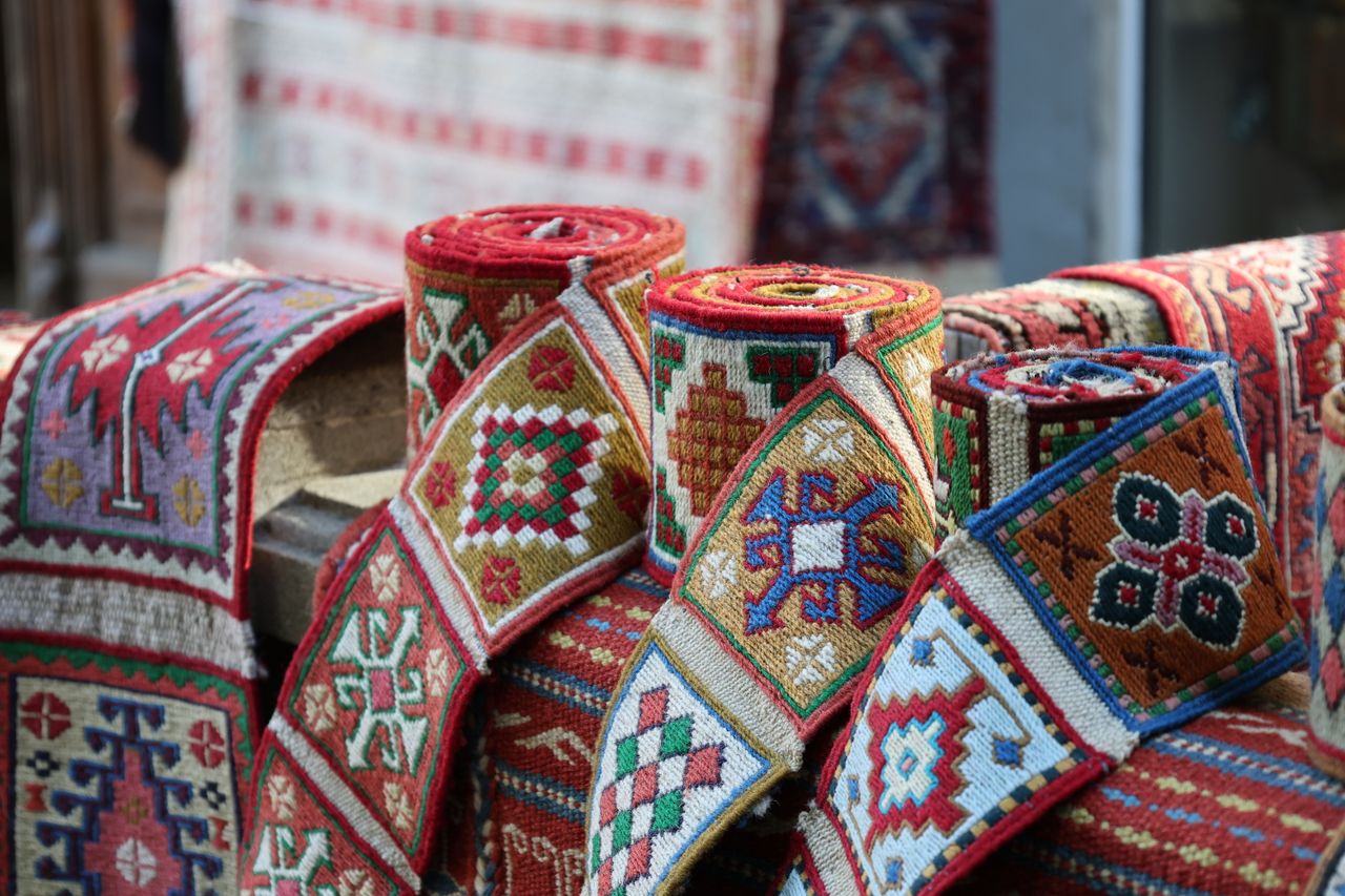 gallery-3 Vibrant rolled textiles featuring geometric patterns in a market setting, showcasing cultural craftsmanship.