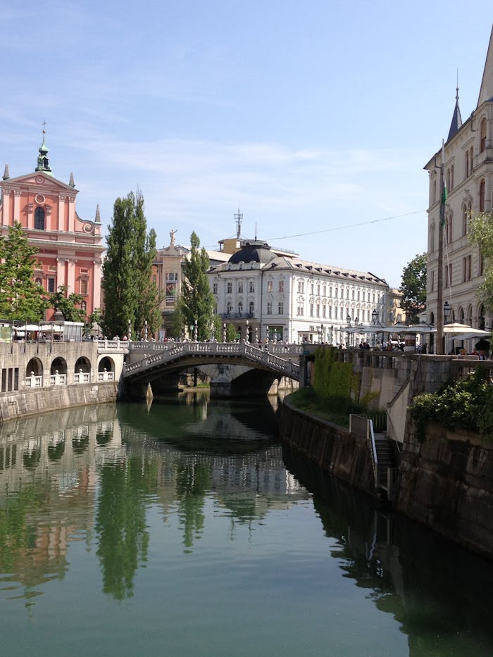 Scenic view of Ljubljana's Triple Bridge and riverfront under clear skies, featuring historic architecture.