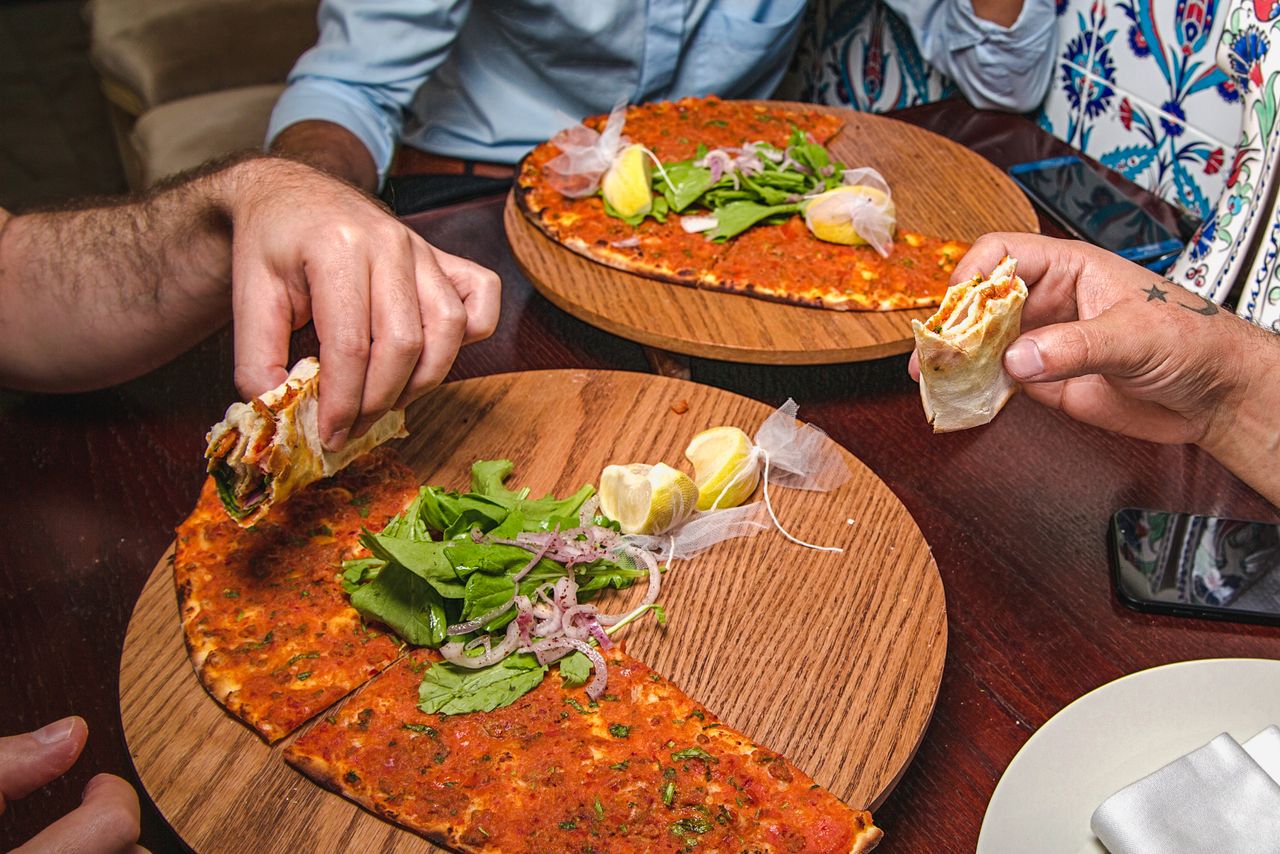 Two people enjoying Lahmacun, a Middle Eastern pizza, at a restaurant in Dubai, UAE.